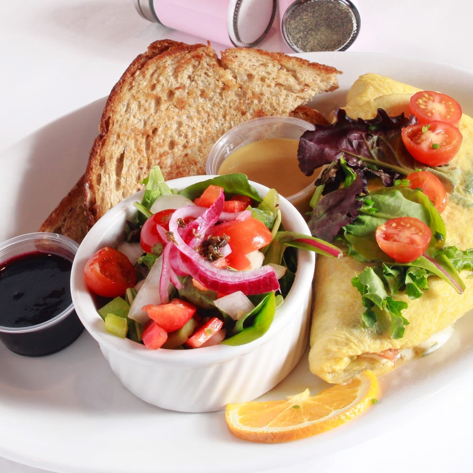 A breakfast plate with an omelet, toast, side salad, and two small cups of sauce.