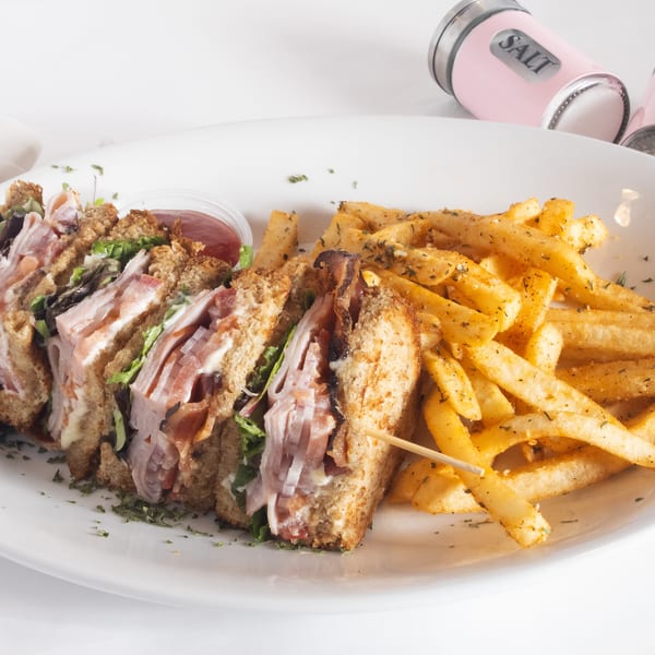 Club sandwich with bacon, lettuce, and tomato, served with seasoned french fries and ketchup.